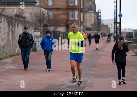 Portobello, Scotland, UK. 28 March, 2020. On the first weekend of the coronavirus lockdown the public were outdoors exercising and maintaining social distancing along Portobello beachfront promenade. Pictured, People walking and jogging on the promenade. Iain Masterton/Alamy Live News Stock Photo