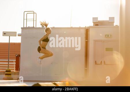 Young woman doing fitness exercise on parking level in the city at sunset Stock Photo