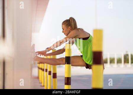 Young woman doing fitness exercise on parking level in the city at sunset Stock Photo