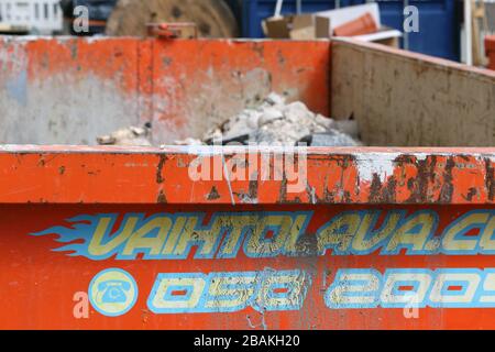 Orange colored dirty and rusty dumpster full of construction waste like broken tiles, cements, etc debris. Photographed in urban area in Helsinki. Stock Photo