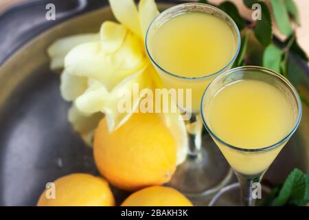 Limoncello in elegant liquor glasses with lemons, mint and yellow rose on steel plate. Sicilian lemon liquor  Stock Photo
