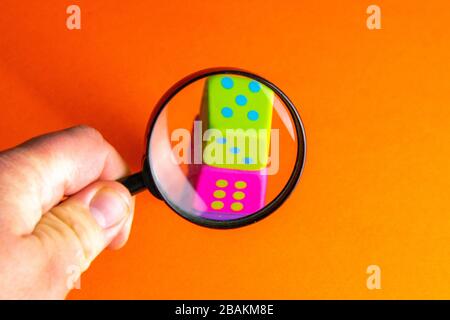 Hand holds magnifying glass over playing cubes. The focus is on the green cube. Search casinos, gambling, fortune Stock Photo