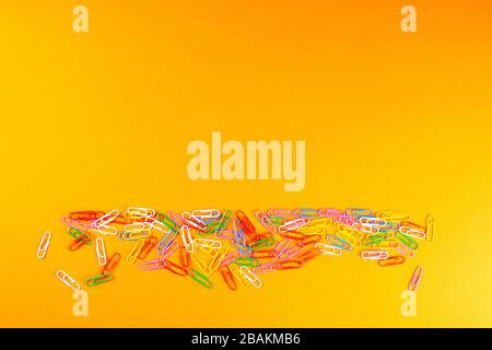 A pile of colored paper clips scattered on a orange surface Stock Photo