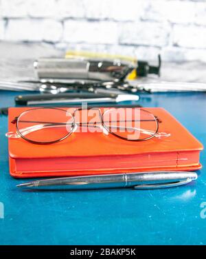 Hairdressing tools set, Red notepad with glasses and scissors, hair clipper, comb, dangerous razor, hair gel stand on blue background Stock Photo