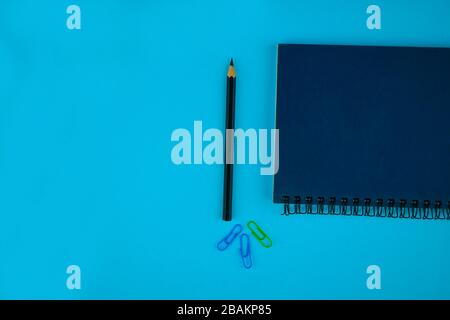 A black pencil crayon,three different colored paper clips on a blue paper background Stock Photo
