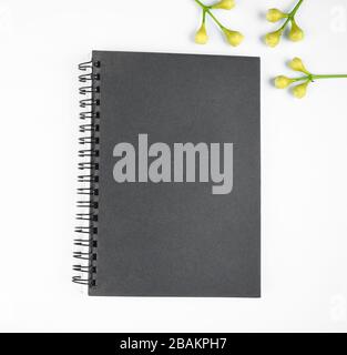 Gray colored paper diary and some small flowers before a bright white background Stock Photo