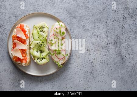 Sandwiches with simple ingredients vegetables, radishes, tomatoes, cucumbers decorated microgreens on gray stone. View from above. Stock Photo