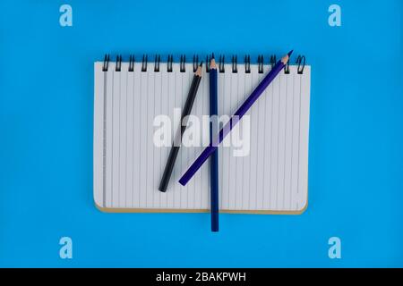 Three different wood pencil crayons scattered on top of a open white paper diary before a light blue paper background Stock Photo
