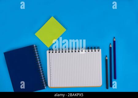 Three wood pencil crayons two diaries and some green sticky notes on a light blue paper background Stock Photo