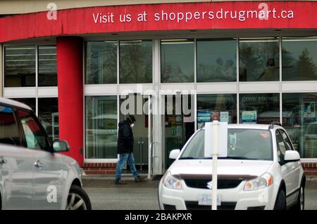 Surrey, B.C, Canada. 27th Mar, 2020. A person is seen wearing a mask as they walk in front of a Shoppers Drug Mart store location, during the COVID-19 pandemic. (Photo by Adrian Brown/Sipa USA) Credit: Sipa USA/Alamy Live News Stock Photo