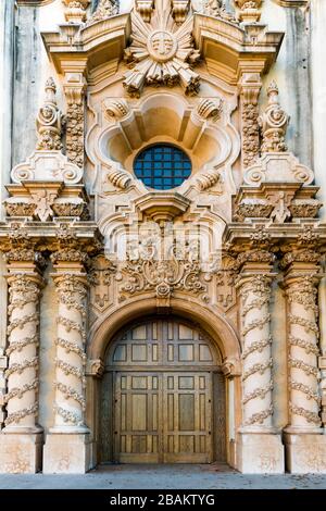 Vertical view of an old building facade with fantastical rococo and baroque architectural elements and an arched oak wood door below a round window Stock Photo
