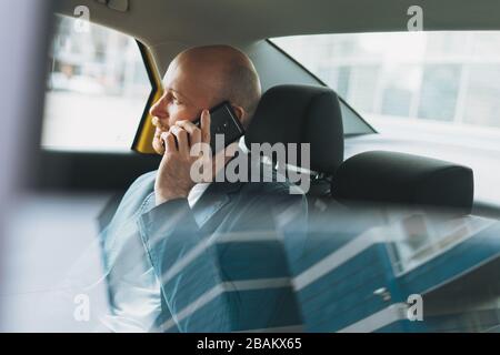 Handsome bald bearded man businessman in suit using mobile phone inside yellow car taxi at city Stock Photo