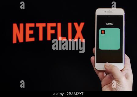 Netflix streaming Service VoD content provider concept. Hand holds before screen a mobile phone with Netflix online watch application logo. Stock Photo