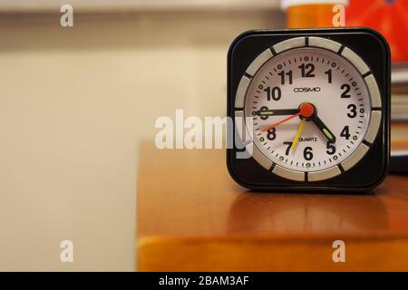 My cheap COSMO travel alarm clock on the bedside table. Current time 4:45pm. Alarm set for 7. Excellent little clock, for the price. Stock Photo
