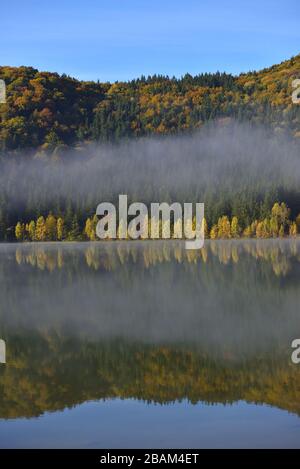 Autumn landscape in the mountains with trees reflecting in the water at St. Ana's lake, Romania Stock Photo