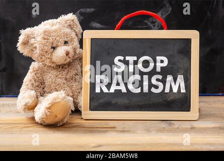 Stop racism and kids concept. Teddy bear and a board with Stop racism text, school class blackboard background. No to racism for children message. Stock Photo