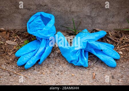 Blue used latex surgical gloves on the ground. Stock Photo