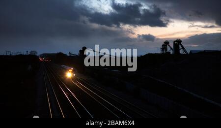 Northern Rail class 170 Turbostar train passing the silhouette of the closed  Hatfield colliery / coal mine, Yorkshire with the headlight glinting. Stock Photo