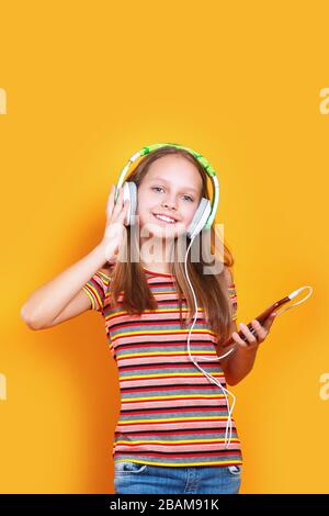 Beautiful little girl in t-shirt listen to music on yellow background Stock Photo
