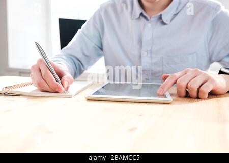 Close-up of unrecognizable marketer sitting at desk and using tablet while working with social medias Stock Photo