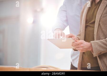 Close-up of unrecognizable businessman using tablet while examining online information with colleague Stock Photo