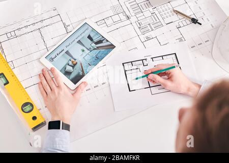 Above view of architect using digital tablet and blueprints while working on floor plan of flat Stock Photo