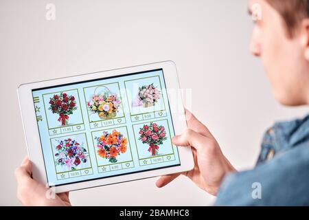 Over shoulder view of young man choosing flower bouquet for girlfriend using catalogue in online store Stock Photo