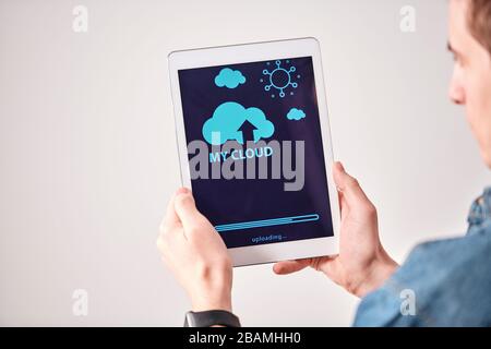 Over shoulder view of young man using digital tablet while uploading files on cloud service Stock Photo