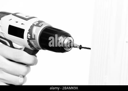 Screwdriver in yellow color held in mans hand near wooden board. Building tool and material isolated on white background, close up and copy space. Repairing and construction concept Stock Photo