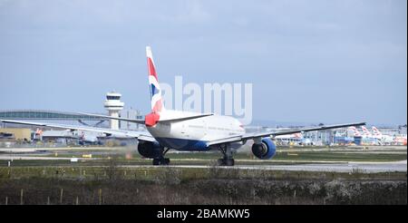 A British Airways Boeing 777-236 callsign G-YMME moves towards the runway for takeoff at Gatwick Airport, passing in front of the air traffic control. Stock Photo