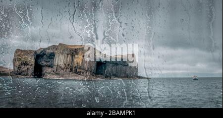 Staffa Island in Scotland through boat window covered in raindrops.