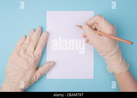 Cropped close up first person view photo of hands in protective white rubber gloves writing on empty paper with a pen isolated on blue background Stock Photo