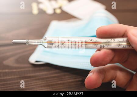 A medical clinical mercury thermometer in person's hand showing the temperature of 39 C. High temperature. wooden background. Theme of health care, me Stock Photo