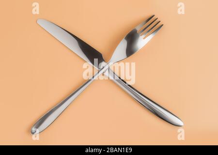 Crossed fork and knife on beige table top view Stock Photo