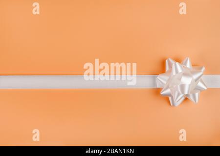 White decorative bow and ribbon on orange background with copy space Stock Photo