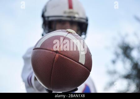 Player holding an American football ball in front of his face. Man hiding behind a ball. Player out of focus and a ball in the foreground Stock Photo