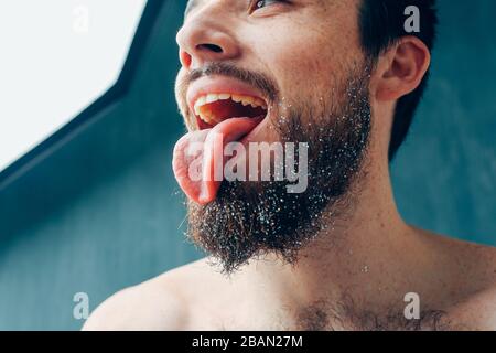 Young man isolated over background. Side low view of guy look left and hold tongue outside of mouth. Stand alone and pose. Cut view and close up. Stock Photo