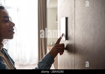 Africanwoman using smart home touch screen technology device on wall. Stock Photo