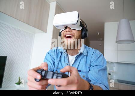 Excited millennial gamer wearing vr glasses hold controller playing video game. Stock Photo