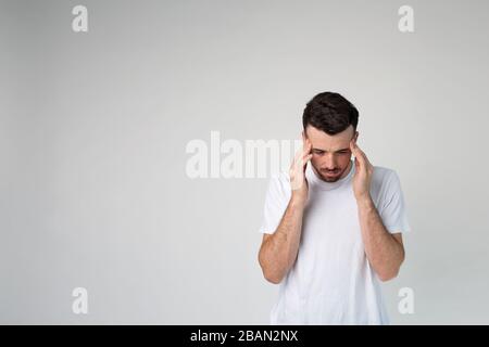 Young man isolated over background. Headache or thinking. Calm peaceful guy in studio stand alone and look down. Stock Photo