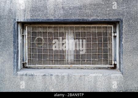 Rectangular basement or cellar window is tightened with wire metal mesh and grille. Technical floor window in the wall of an old gray building. Stock Photo