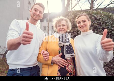 Two helpers of social service and senior lady giving thumbs up Stock Photo