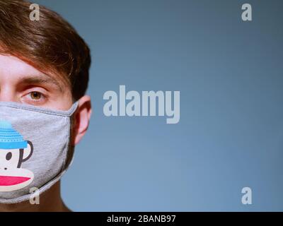 Closeup of a caucasian man face wearing funny monkey face protection mask with a brown eyes and hair, since new coronavirus outbreak. Stock Photo