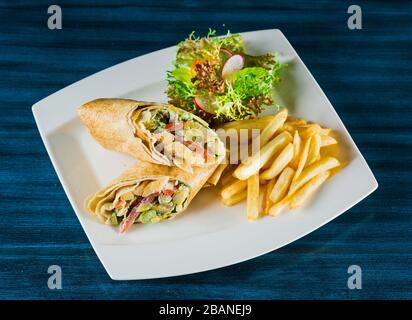 Shawarma chicken roll in a pita with fresh vegetables and cream sauce on wooden background. Selective focus. Stock Photo