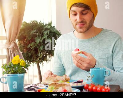 Beautiful colourful spring breakfast setting with a variety of food on a wooden table with flowers on a sunny day and man sitting in the balcony. Stock Photo