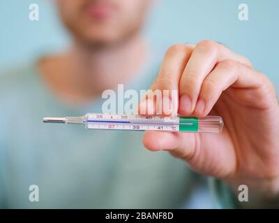 Closeup of a man holding a thermometer for measuring body temperature degrees Celsius at 38,5 background. Stock Photo