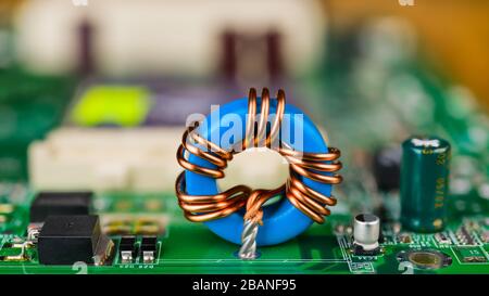 Blue toroidal induction coil on green circuit board. Computer mainboard detail. Electronic components. Ferrite core inductor, capacitor or transistor. Stock Photo