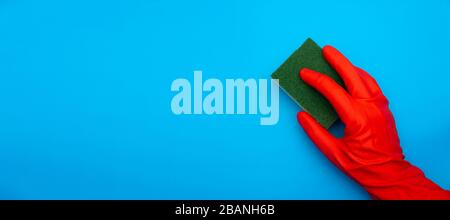concept image of hand in red rubber protecting glove holding sponge with green fiber isolated on classic blue background