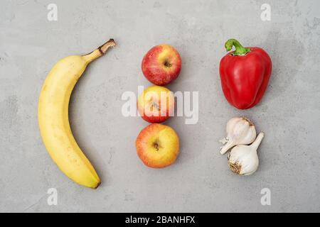 Natural, natural looking fruits and vegetables, on a grey concrete background. Banana, Apple, pepper and garlic.Raw unprocessed foods and vitamins. Stock Photo