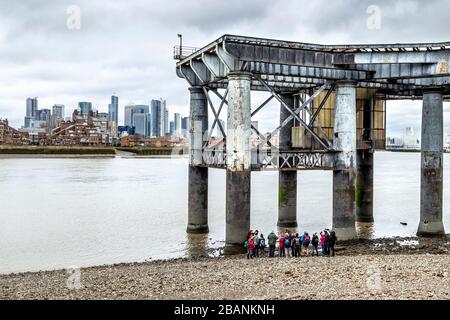 A tour group standing on the Thames riverbank by the old coal jetty of Greenwich Power Station, Crowley's Wharf, Greenwich, London, UK Stock Photo